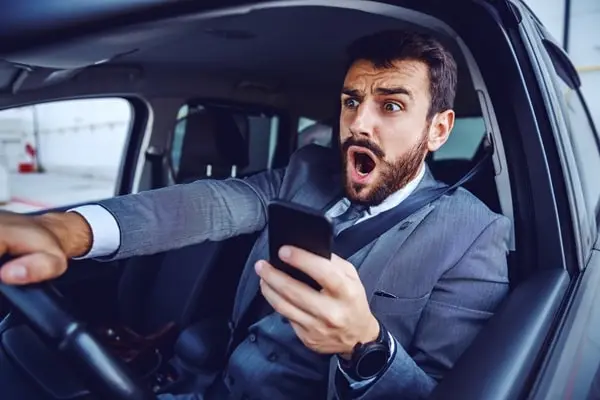 Ein Autofahrer benutzt sein Smartphone während der Fahrt und erschrickt sich.